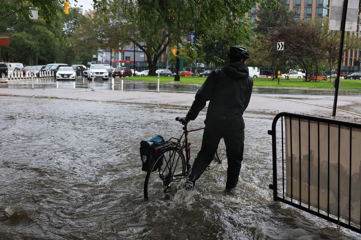 2023 年 9 月 29 日，在纽约市布鲁克林的弗拉特布什社区，在一场沿海风暴中，一个人骑着自行车沿着展望公园附近一条被洪水淹没的道路穿过齐踝深的水中。